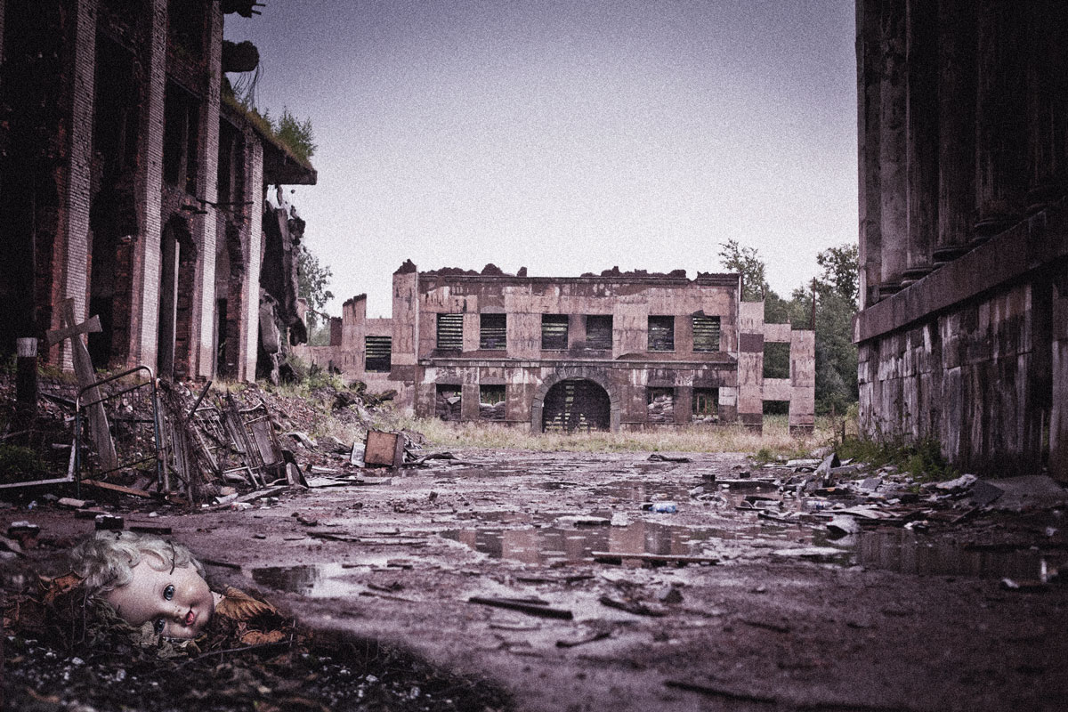 An indigo-tinged photo of a ruined factory floor, with a doll’s head lying in the rubble in the foreground.
